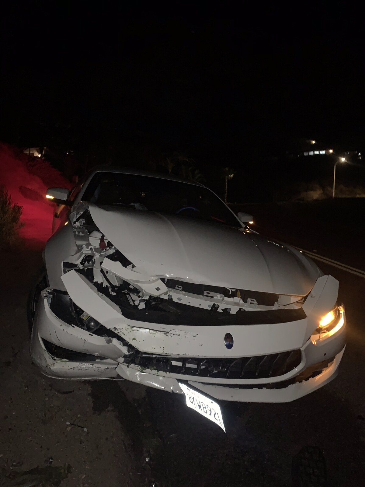 A white Maserati with its front end crushed after a night crash